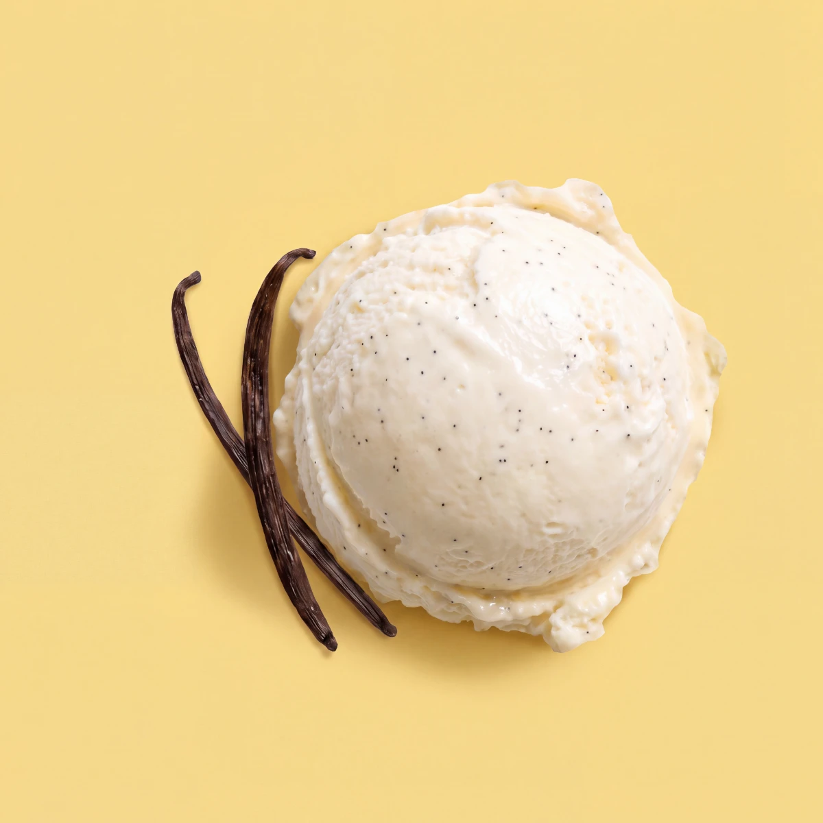 Top-down scoop of vanilla bean ice cream with vanilla pods on a vanilla-yellow backdrop