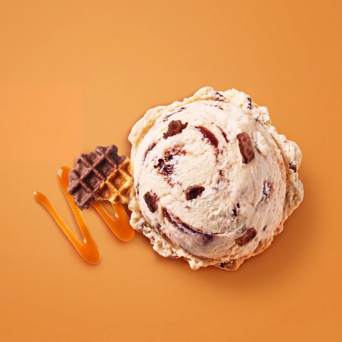 Top-down scoop of choco caramel waffle ice cream with waffle and caramel on an orange backdrop
