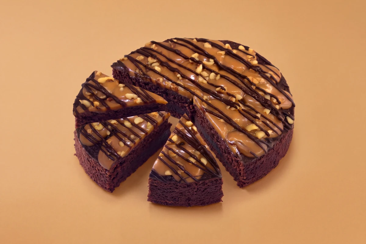 Chocolate cake with caramel drizzle and pecans, sliced, on a caramel backdrop