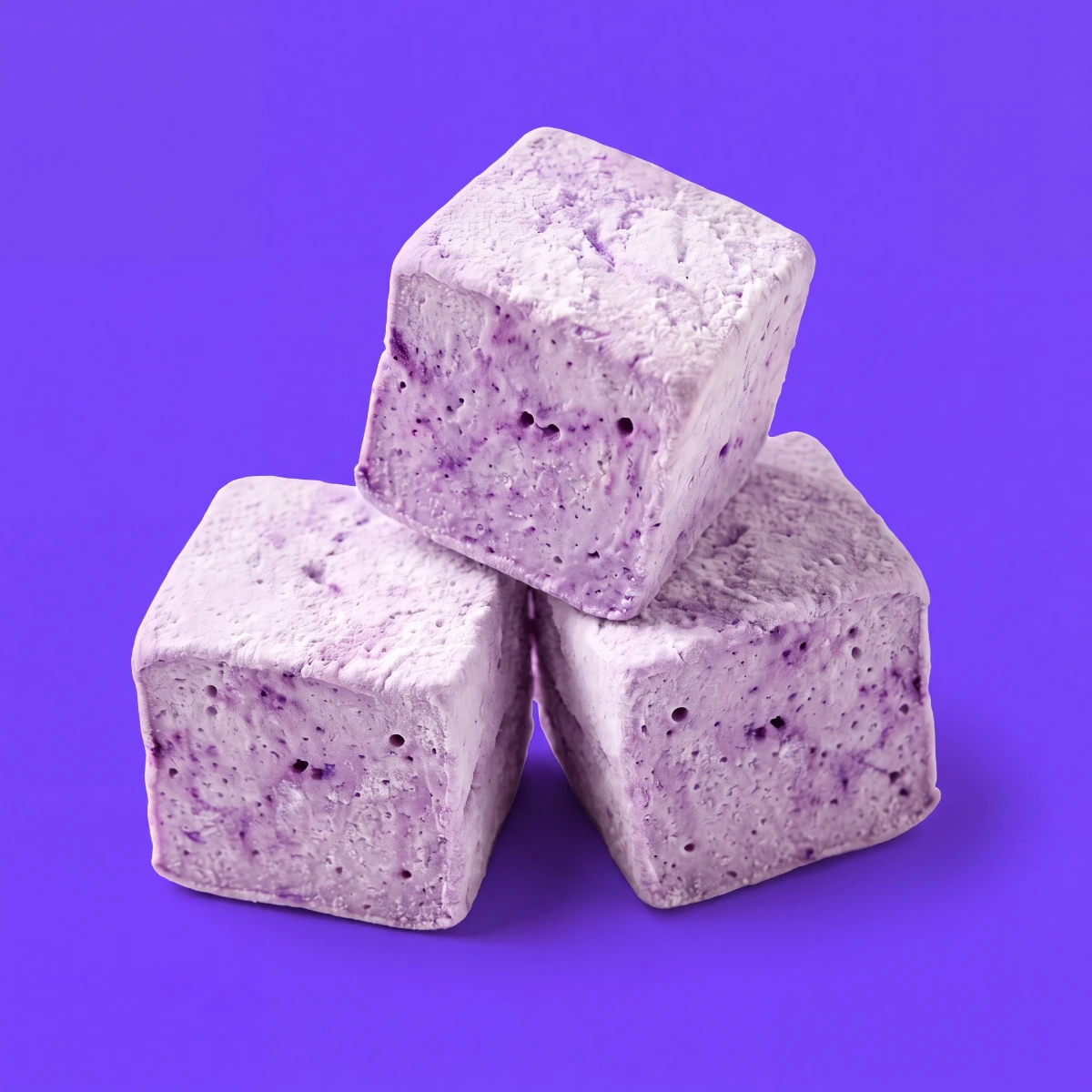 Three ube marshmallow cubes on a violet backdrop